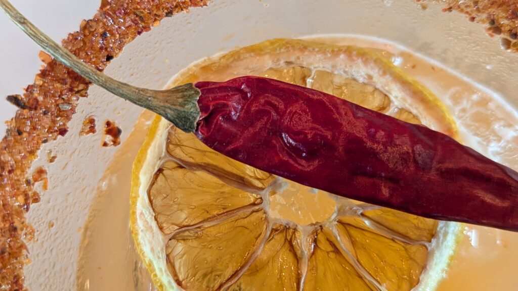 Close up of drink with salted rim, lemon, and red chili pepper