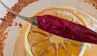 Close up of drink with salted rim, lemon, and red chili pepper