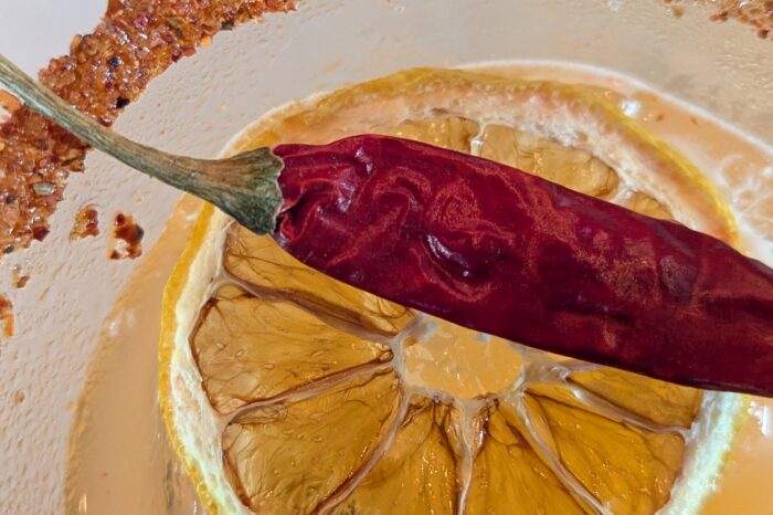 Close up of drink with salted rim, lemon, and red chili pepper